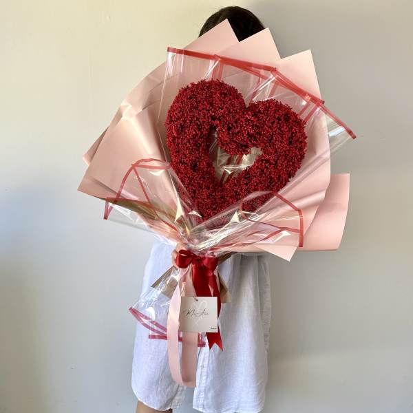 Heart-shaped red flower bouquet wrapped in pink paper and clear plastic