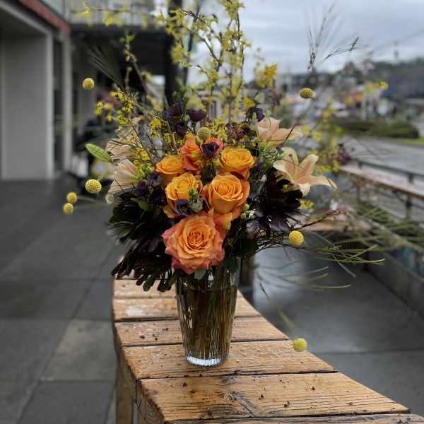 Orange roses in a clear glass vase with airy yellow accents