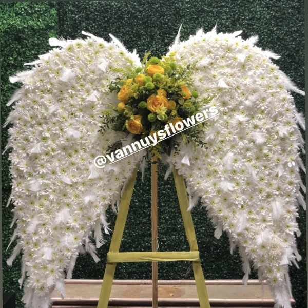 Standing angel wing spray of white flowers with yellow and green bouquet center on wooden easel