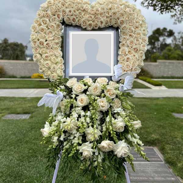 Standing floral tribute with cream roses around a framed photo and white doves