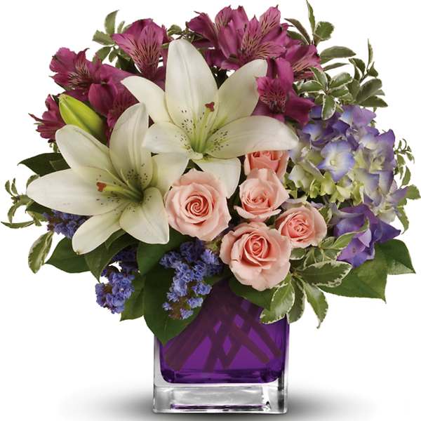 Bouquet of white lilies, pink roses, and purple flowers in a glass vase