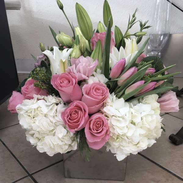 Pink roses and white lilies in a square glass vase with white hydrangeas