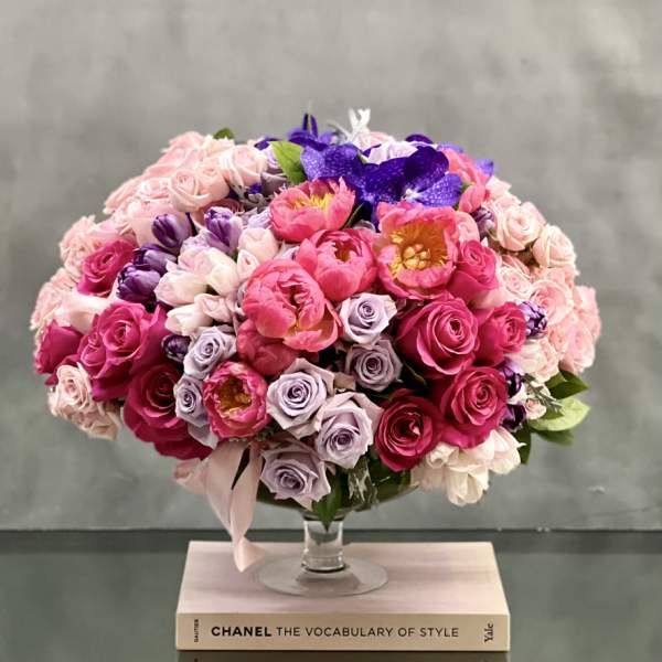 Round bouquet of pink, lavender, and purple flowers in a glass vase.