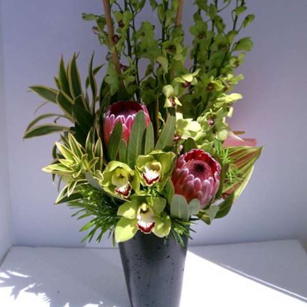 Tall modern arrangement with green orchids and pink protea in a black vase with vertical bamboo sticks