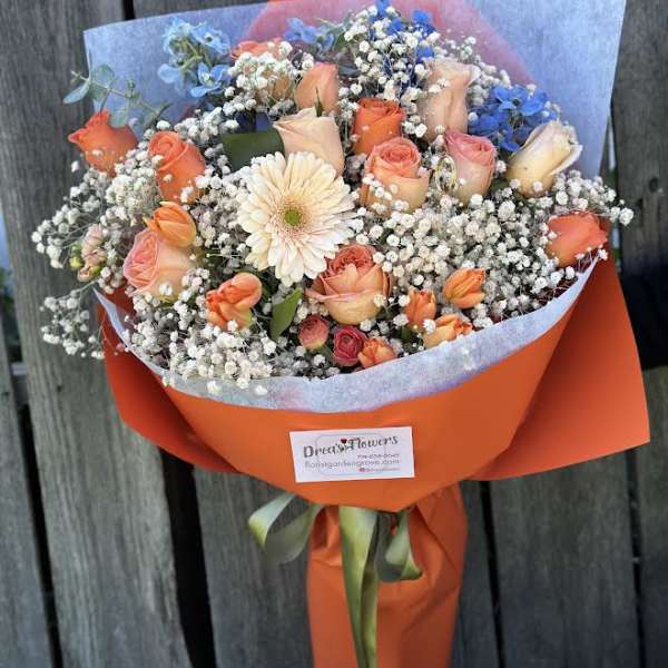 Bouquet of peach roses, blue flowers, and white baby's breath wrapped in orange paper