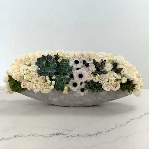 Low floral arrangement of cream roses, white anemones, and succulents in a gray container