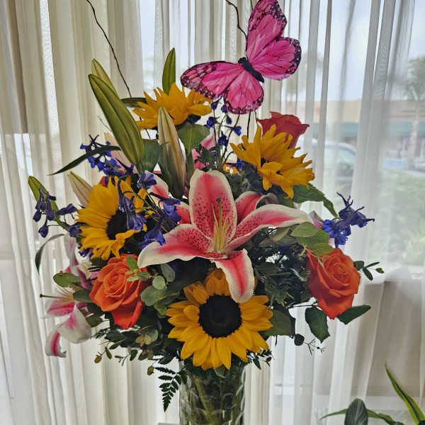 Bright mixed bouquet in a glass vase with a pink butterfly pick