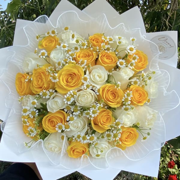 Bouquet of yellow and white roses with small daisy flowers wrapped in white paper