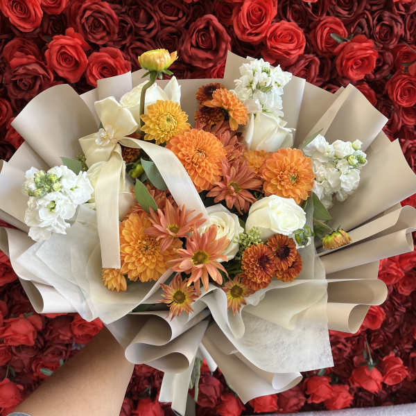 Bouquet of orange, white, and cream flowers wrapped in beige paper