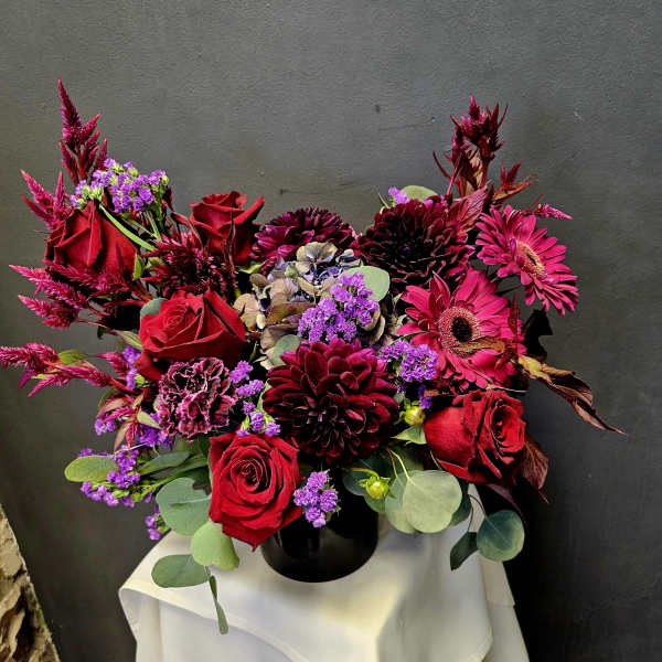 Red roses and magenta flowers arranged in a black vase