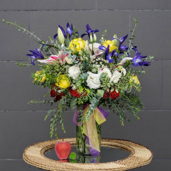 Mixed bouquet of yellow, white, pink, and purple flowers in a glass vase