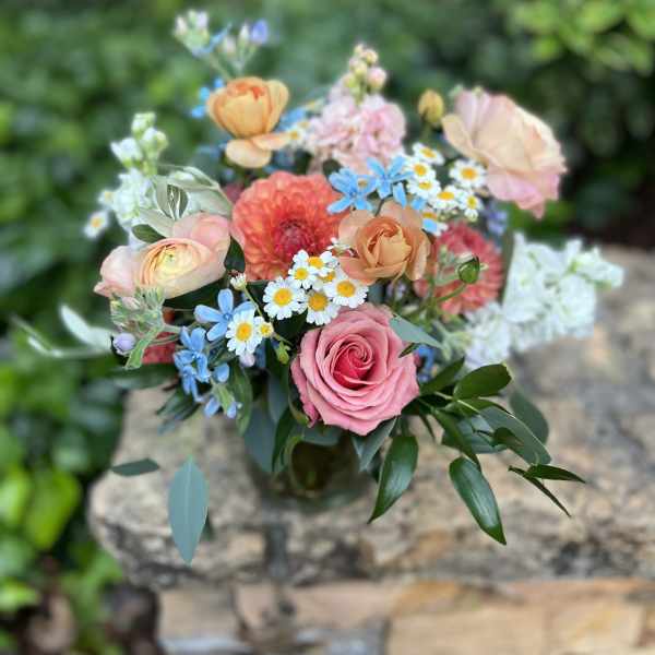 Mixed bouquet of pink, peach, and blue flowers in a glass vase