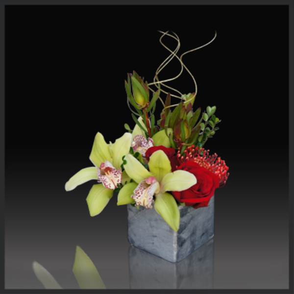 Red roses and pale green orchids in a square gray vase