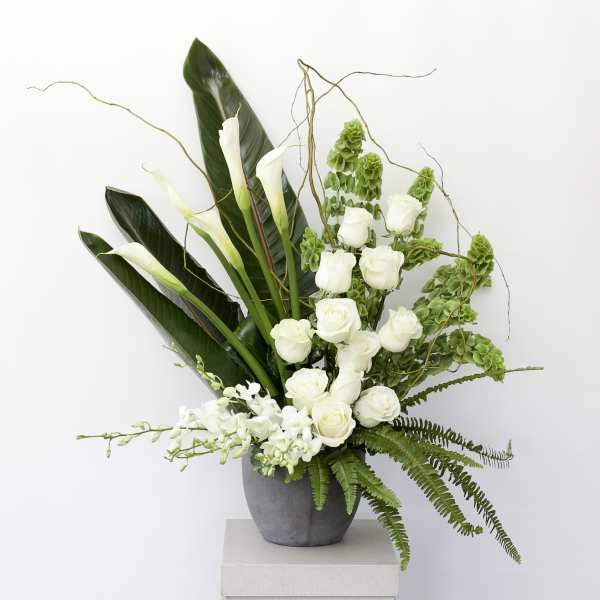 White roses and calla lilies in a gray vase with green foliage