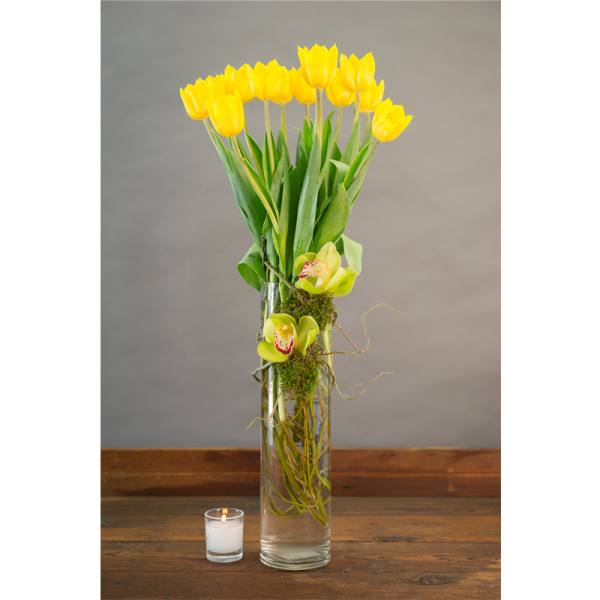 Yellow tulips in a tall glass vase with two green orchids and a small candle