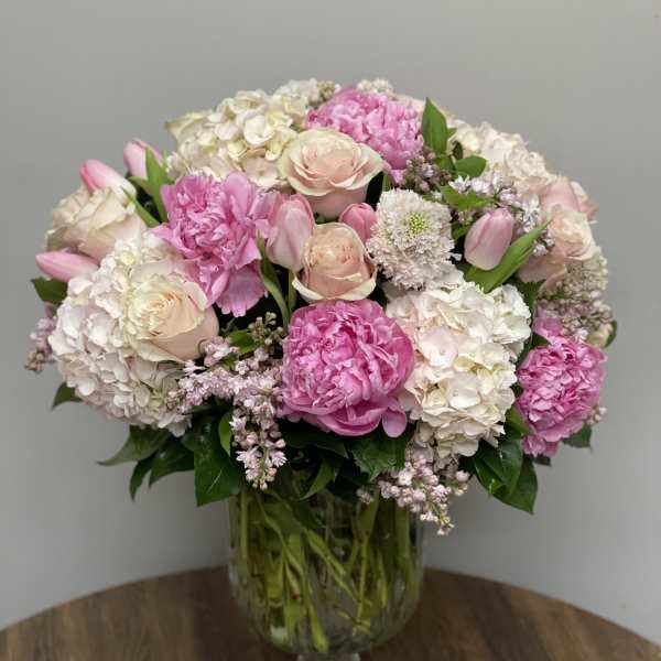 Large pink and white arrangement of peonies, roses, tulips and hydrangeas in a clear glass vase