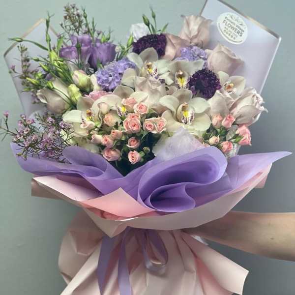 Bouquet of pastel orchids, roses, and purple blooms wrapped in lavender paper