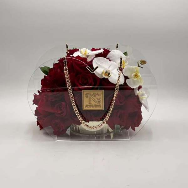 Red roses and white orchids in a clear round handbag-style container