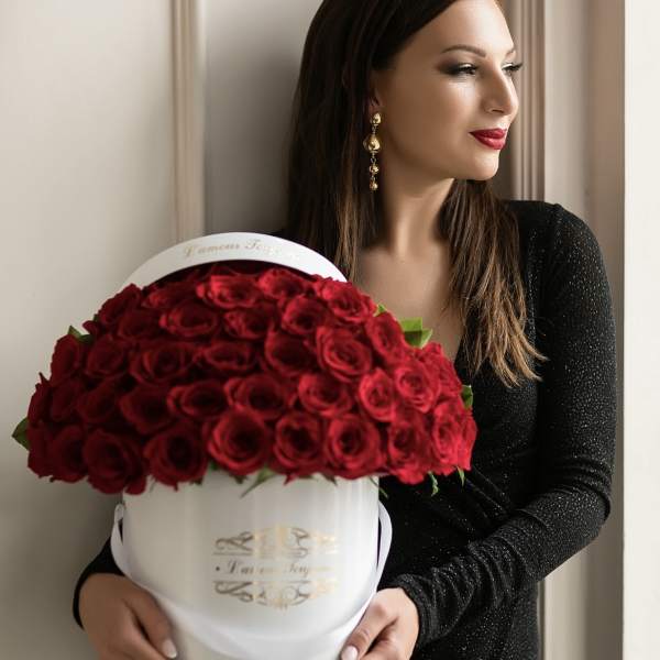 Woman in a black dress holding a round white box filled with dozens of red roses.