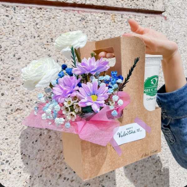Bouquet of white and purple flowers in a kraft gift bag with a drink cup