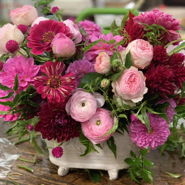 Pink and magenta mixed flowers arranged in a white footed vase