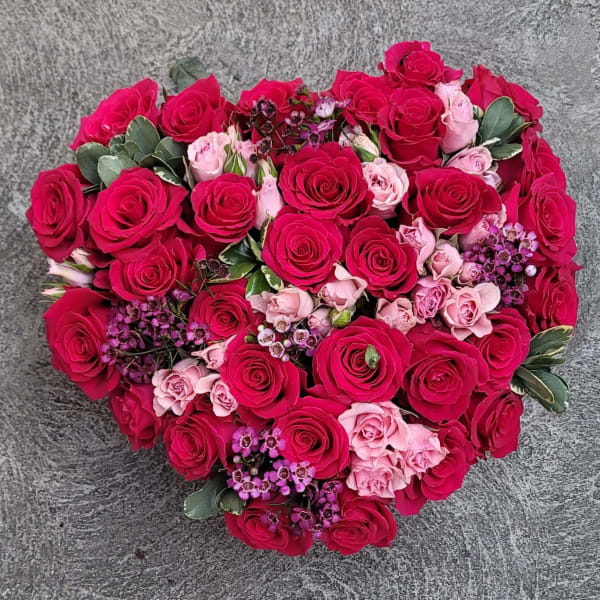 Heart-shaped bouquet of pink and red roses with small purple accents