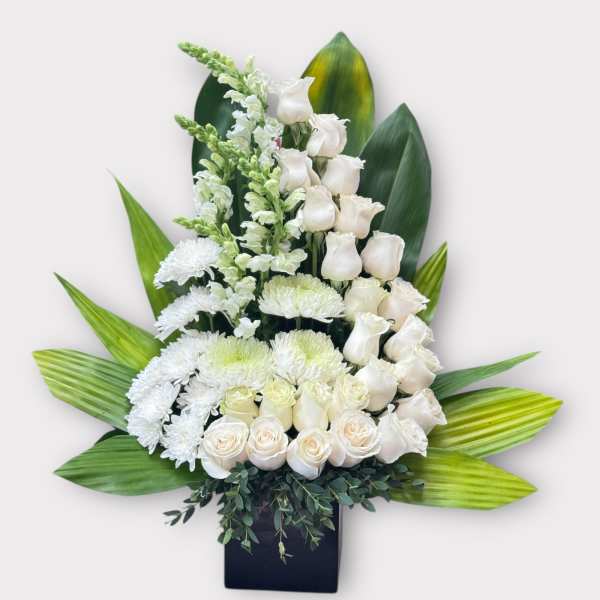 White roses and chrysanthemums arranged in a black vase with large green leaves.