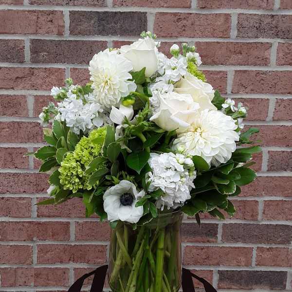 White floral arrangement in a glass vase with green accents