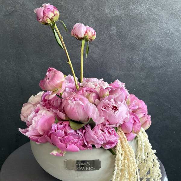 Pink peonies arranged in a white oval container with trailing cream flowers