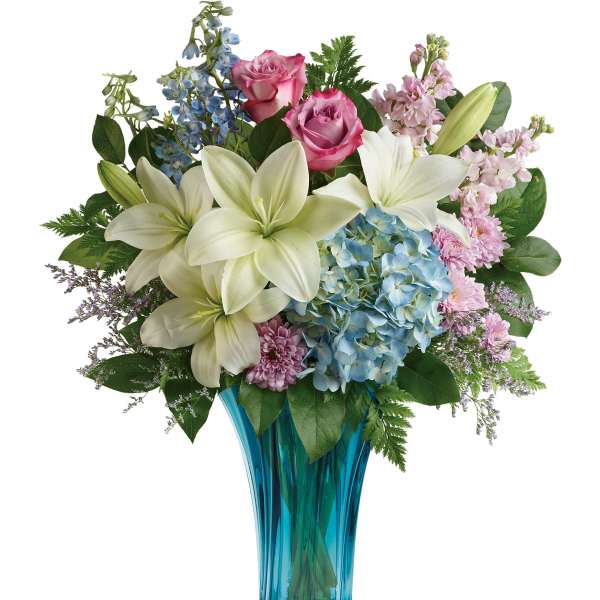 Bouquet of white lilies, pink roses, and blue hydrangeas in a blue glass vase