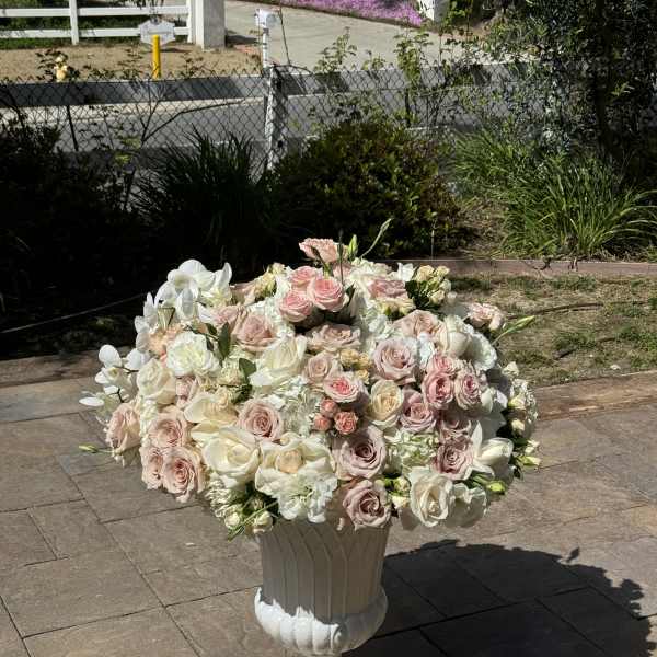 Large pastel rose arrangement in a white pedestal urn