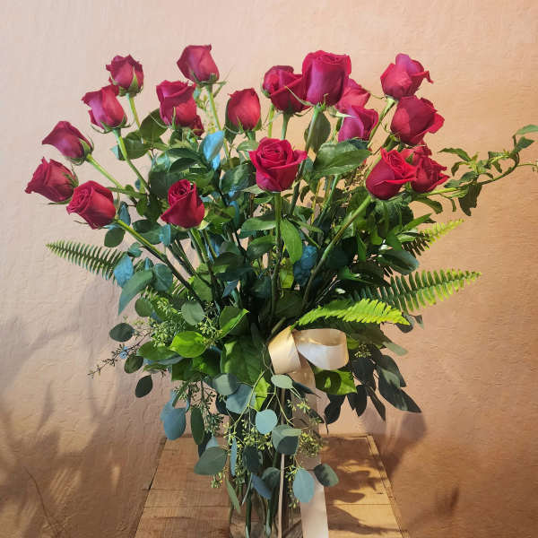 Tall bouquet of red roses in a clear glass vase with a ribbon