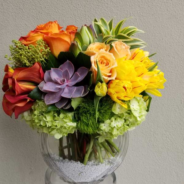 Mixed bouquet with orange roses, yellow tulips, and a purple succulent in a glass vase