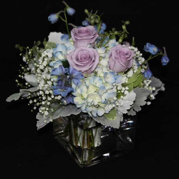 Lavender roses and blue hydrangeas in a clear glass vase