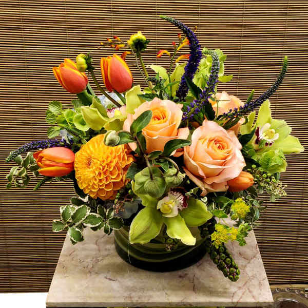 Mixed bouquet with peach roses, orange tulips, and green orchids in a glass vase