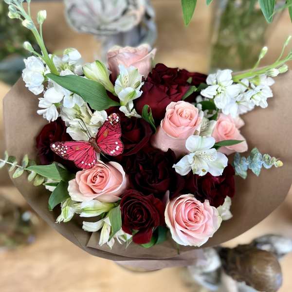 Bouquet of pink and deep red roses with white flowers wrapped in brown paper