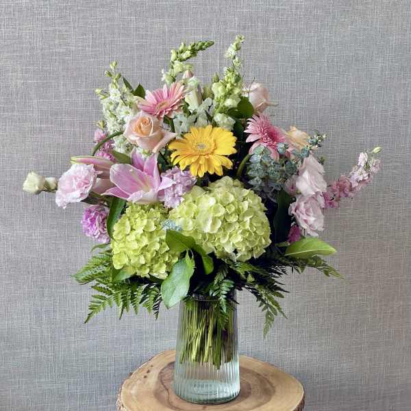 Mixed bouquet with pink, yellow, and green flowers in a glass vase