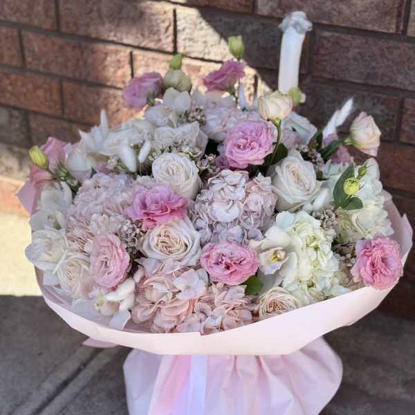 Pink and white bouquet of roses, hydrangeas, and carnations wrapped in pale pink paper