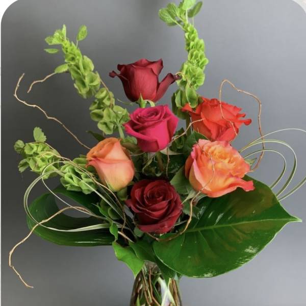 Mixed roses in a clear glass vase with curly greenery