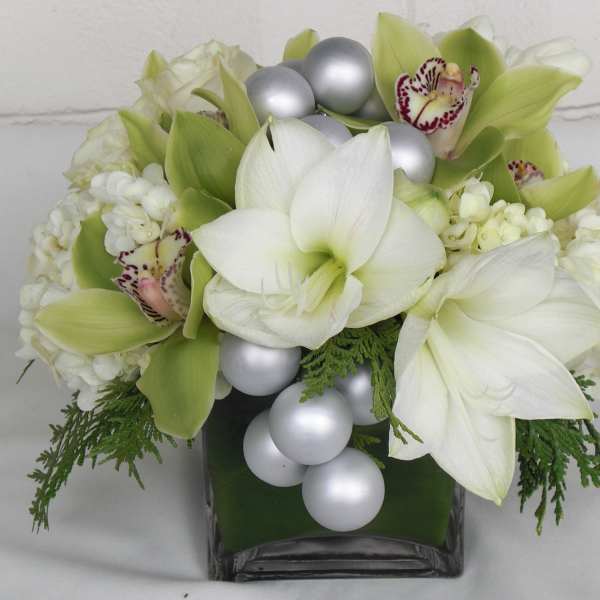 White and green floral arrangement in a square glass vase with silver ornaments