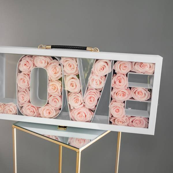 White box sign spelling LOVE filled with pale pink roses