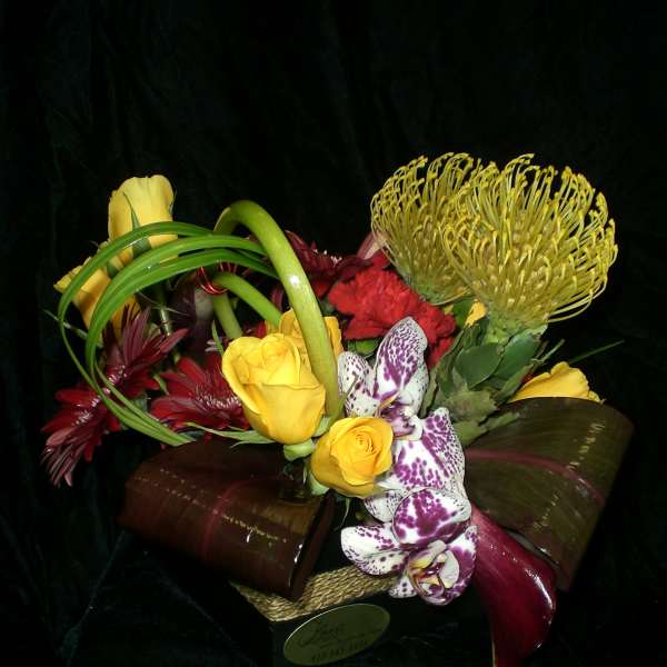 Mixed bouquet with yellow roses, orchids, and red flowers in a low container