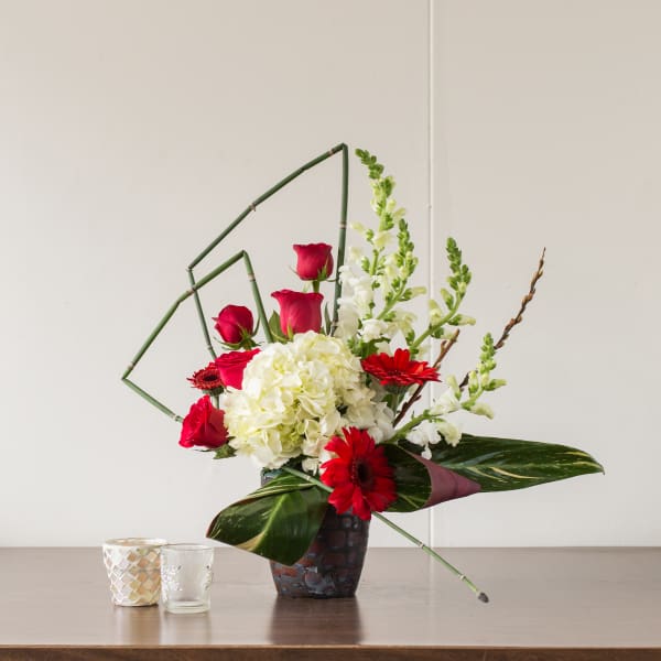 Red roses and gerbera daisies in a dark vase with white hydrangea