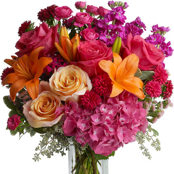 Mixed bouquet of roses, lilies, hydrangea, and mums in a clear glass vase