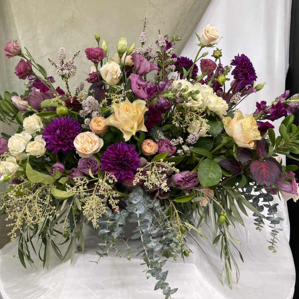 Large bouquet of purple, pink, and cream flowers with trailing greenery