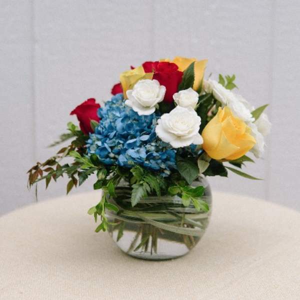 Bouquet of red, yellow, white, and blue flowers in a glass vase