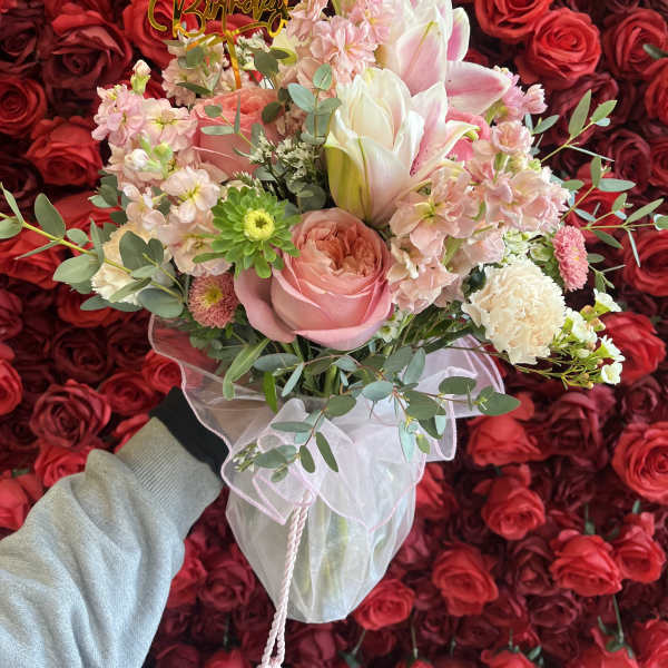 Pink and white bouquet with a birthday topper against a wall of red roses
