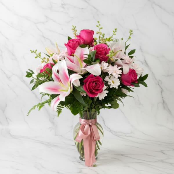 Pink roses and lilies in a glass vase with a pink ribbon
