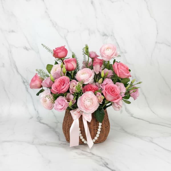 Pink rose and ranunculus arrangement in a wicker basket with a ribbon