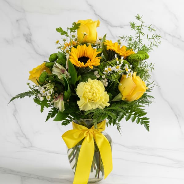 Yellow roses and mixed flowers in a glass vase with a yellow ribbon
